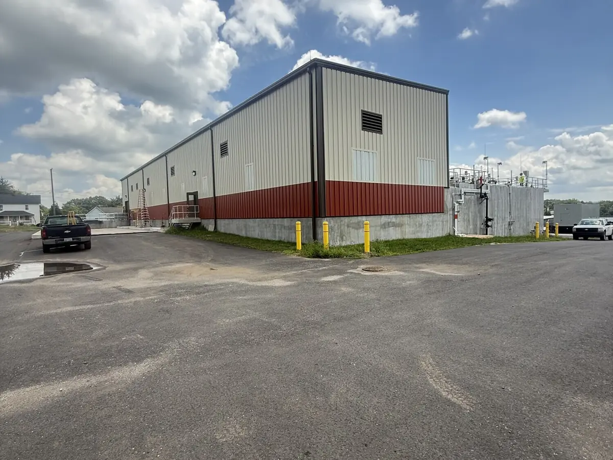 A completed metal warehouse with white cladding and a red accent band, finished parking apron