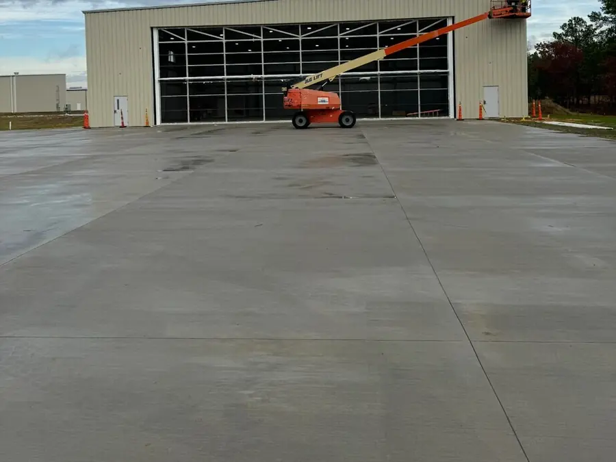A finished metal building with a tall roller door and a boom lift parked on the concrete apron