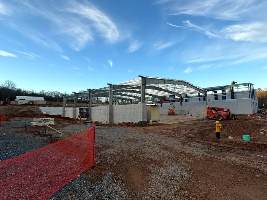 A steel frame standing on a prepared pad with cladding started, safety fencing around the working area