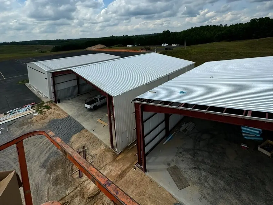 Two open-sided metal structures with red steel columns on a finished concrete pad